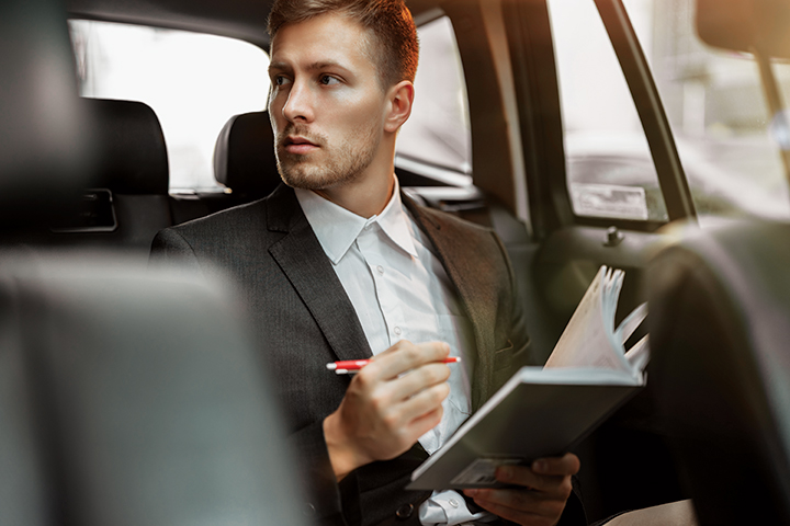 Man writing in a notebook in the back seat of a vehicle