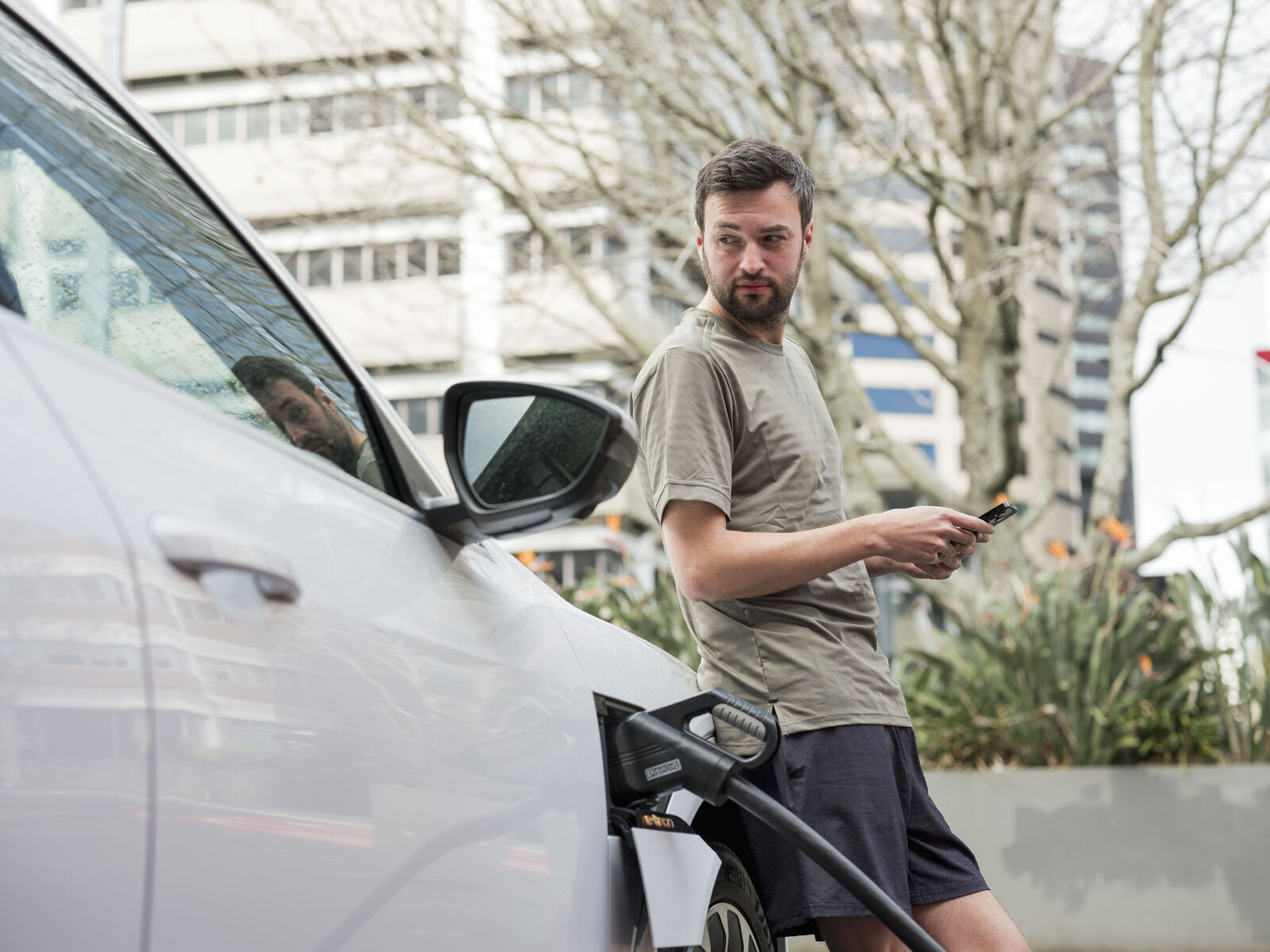 Man waiting for EV to charge at charging station in Auckland