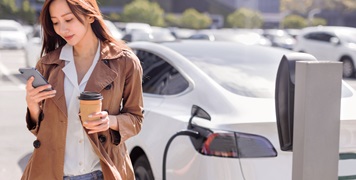 Woman on phone holding coffee waiting for her EV to charge