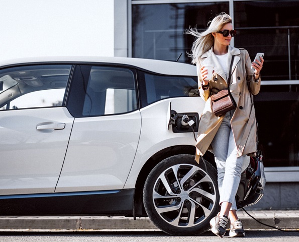 Woman leaning on her business vehicle while it charges