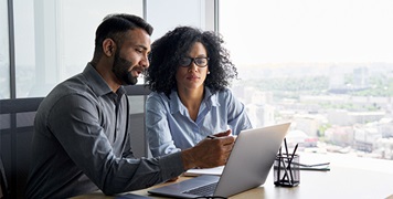 Two colleagues reviewing information on a laptop