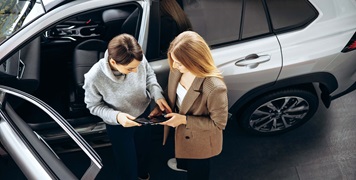 Two people standing outside car with a tablet