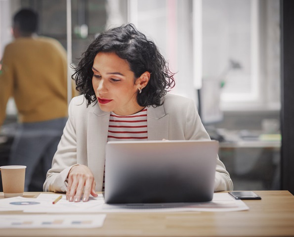 business-woman-sitting-at-desk-in-front-of-laptop-reviewing-paperwork