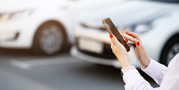 close-up-of-womans-hands-using-mobile-phone-standing-near-car-rentals