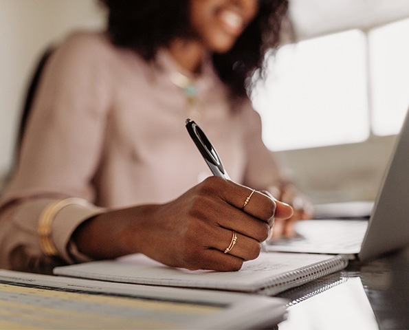 female-holding-pen-to-paper-sitting-in-front-of-laptop female-holding-pen-to-paper-sitting-in-front-of-laptop