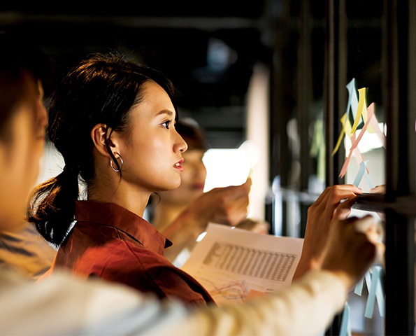 female-professional-brainstorming-looking-at-post-it-notes-in-office-setting female-professional-brainstorming-looking-at-post-it-notes-in-office-setting