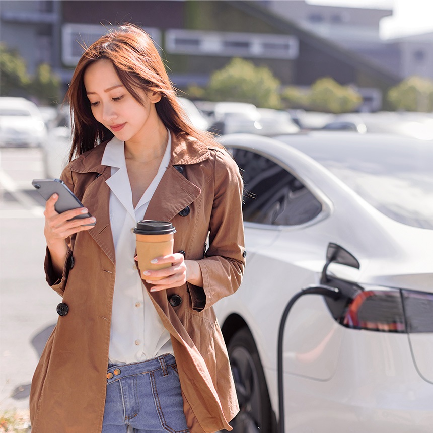 woman-in-car-park-looking-at-phone-in-front-of-an-electric-car-charging