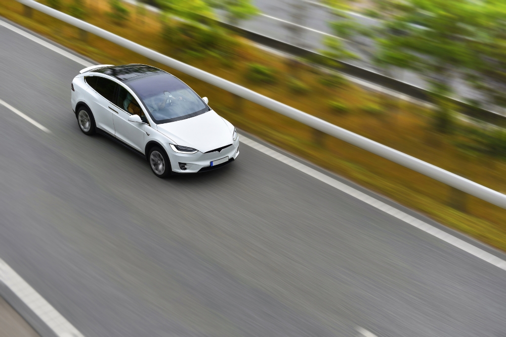 White electric car driving on an open road, reflecting motoring trends and cost changes linked to the 2025 Budget.