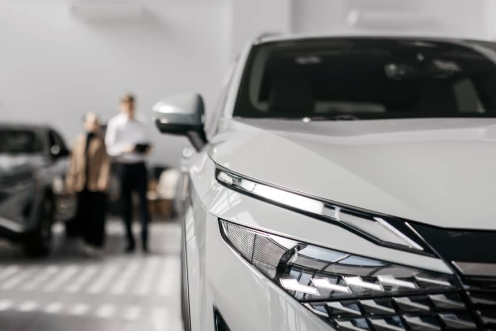White car displayed in a showroom with customers in the background, representing fleet company access to multiple car manufacturers and OEM options.