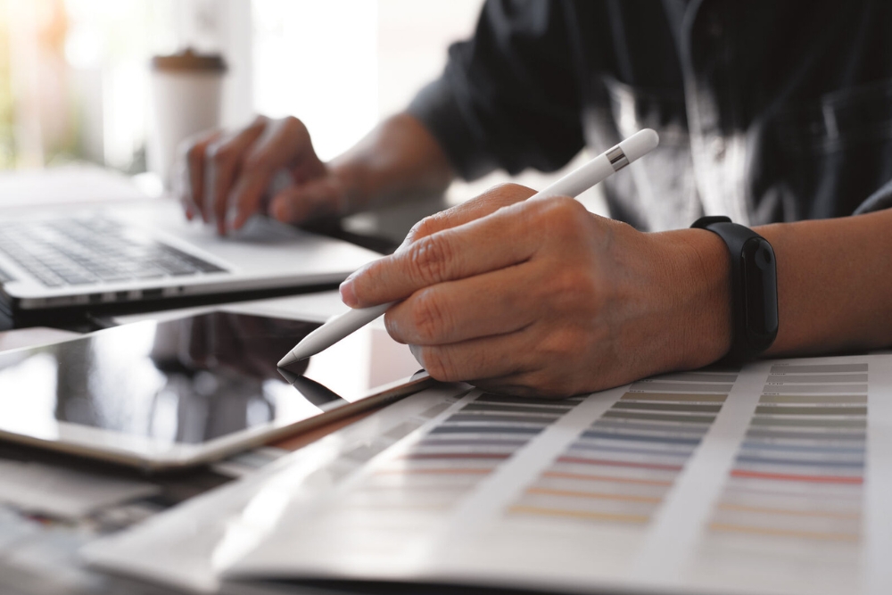 Close-up of a person using a stylus on a tablet while working on a laptop, with a colour chart in the foreground—illustrating admin work for managing a growing vehicle fleet.