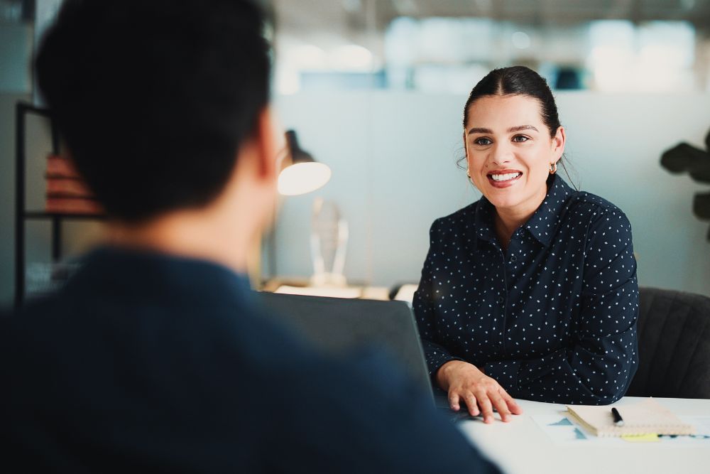 best places to work SG Fleet: A smiling woman in a navy polka-dot blouse sits across a desk from a colleague in a bright, modern office.