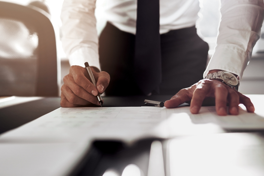Businessman in formal attire reviewing and signing car leasing paperwork at a desk, representing the process of leasing a company vehicle.