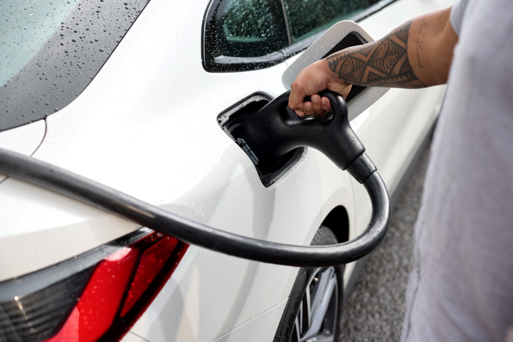 Person charging a white electric car in the rain, symbolising the practical side of electric vehicle ownership or leasing.