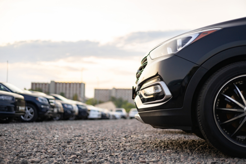EV Fleet maintenance: Several cars parked in a row on gravel with a close-up view of the front wheel of a black vehicle.