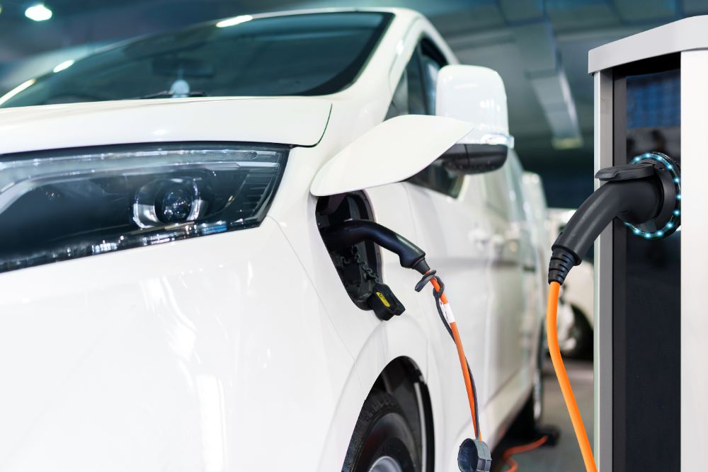 Grey fleet duty of care risks in the UK: A close-up of an orange charging cable connected to the charge port of a white electric vehicle at a charging station.