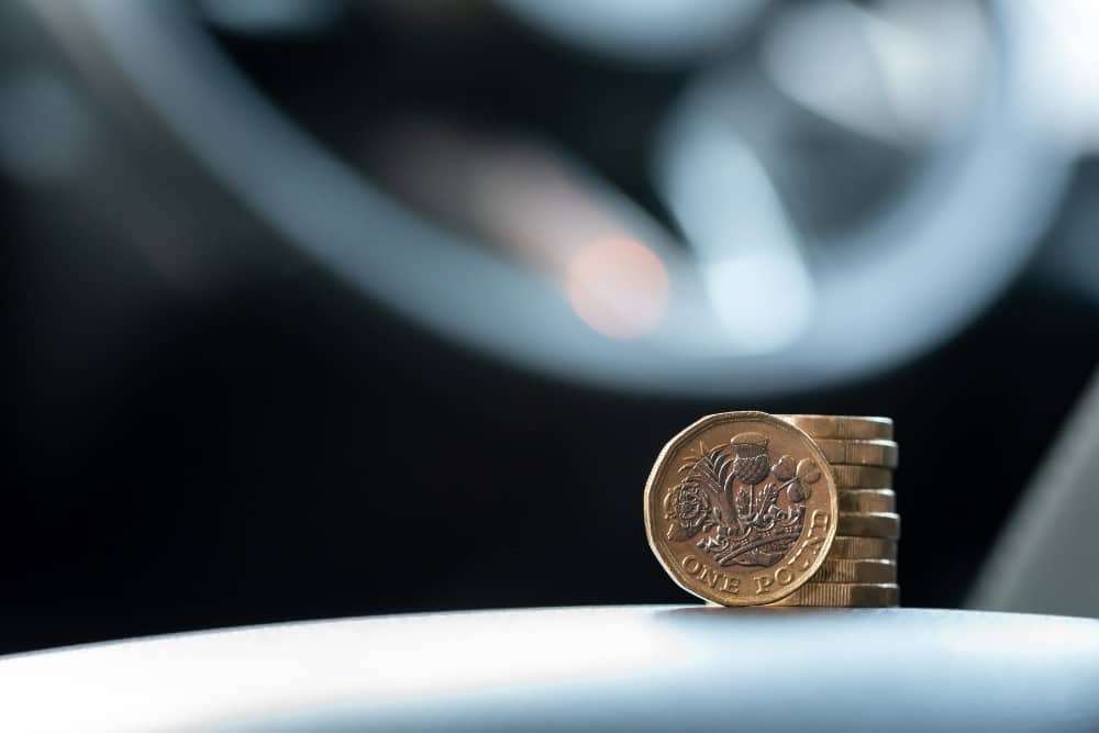Stacked pound coins in front of blurred car steering wheel