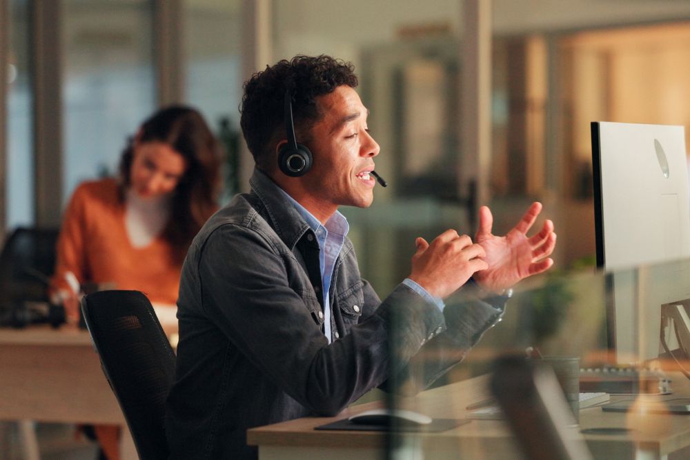 SG Fleet places to work employees: A man wearing a headset speaks animatedly at his desk in a modern open-plan office, with a colleague working in the background.