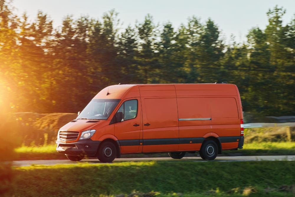 Vehicle downtime Orange delivery van driving on a rural road, representing vehicle use and potential downtime impacts
