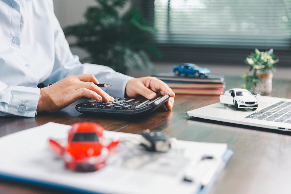 Workplace car benefits Person using calculator with model cars and laptop, representing workplace car benefits and financial planning